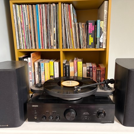 A record player, amp & turntables, in front of a Kallax containing records and music books